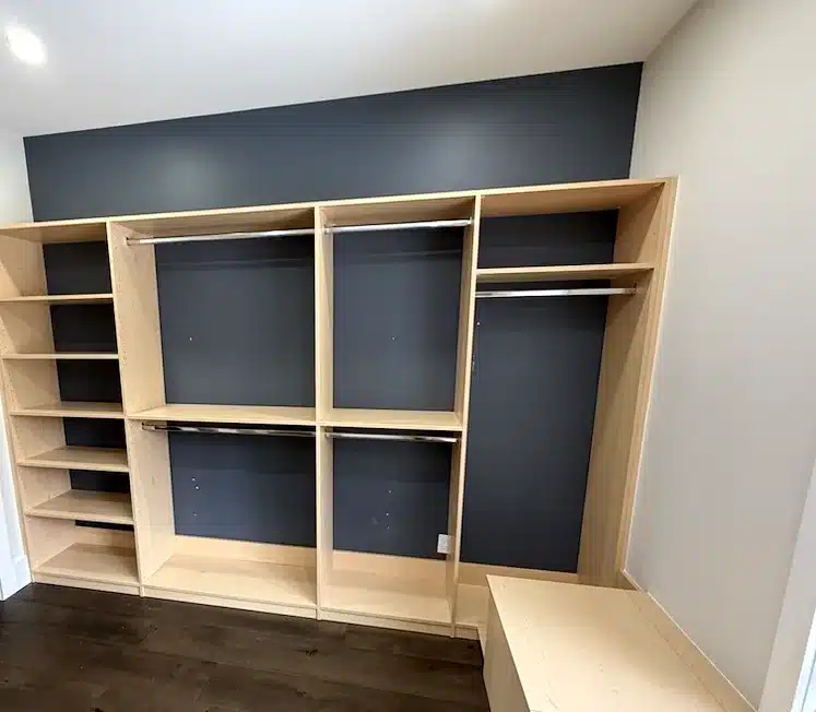Custom closet design in an Ontario home: a maple walk-in with navy back panels, high-low hanging and a built-in window bench.