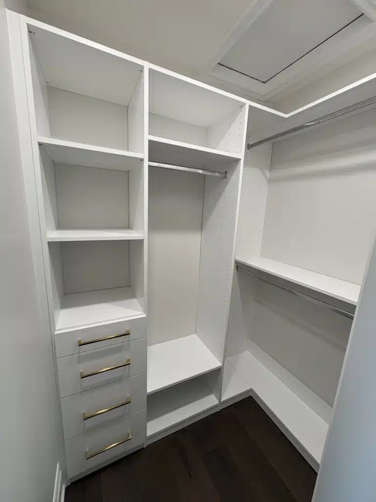 Custom closets in an Ontario home: a walk-in with a four-drawer tower on brass pulls, open shelving above and long hanging opposite.