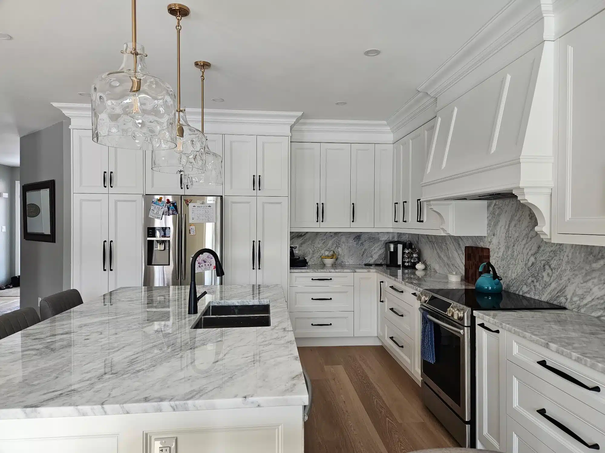 Custom kitchen cabinets in an Ontario home: white shaker doors, a full-height marble-look island and brass pendant lighting.