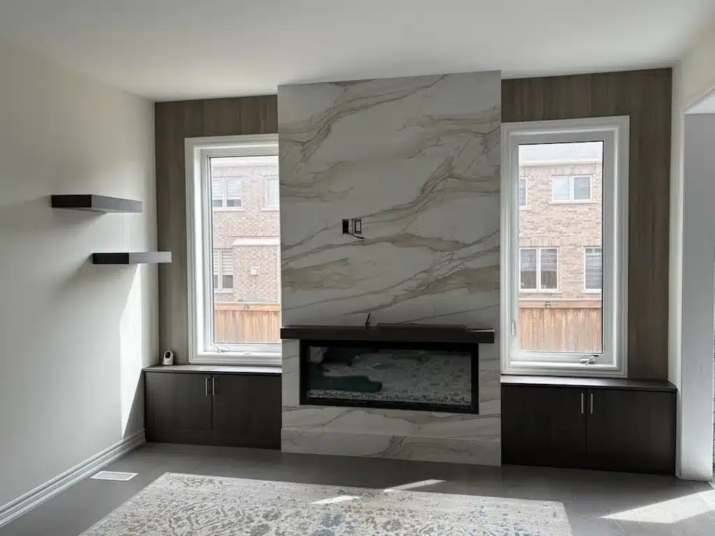 A built-in fireplace wall with a stone slab surround, dark flanking base cabinets and floating shelves in an empty Ontario room.