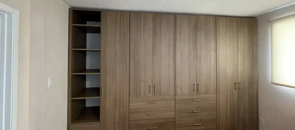 A built-in wardrobe wall in an oak-look finish in an Ontario bedroom, with an open shelf tower beside tall door bays and drawers.