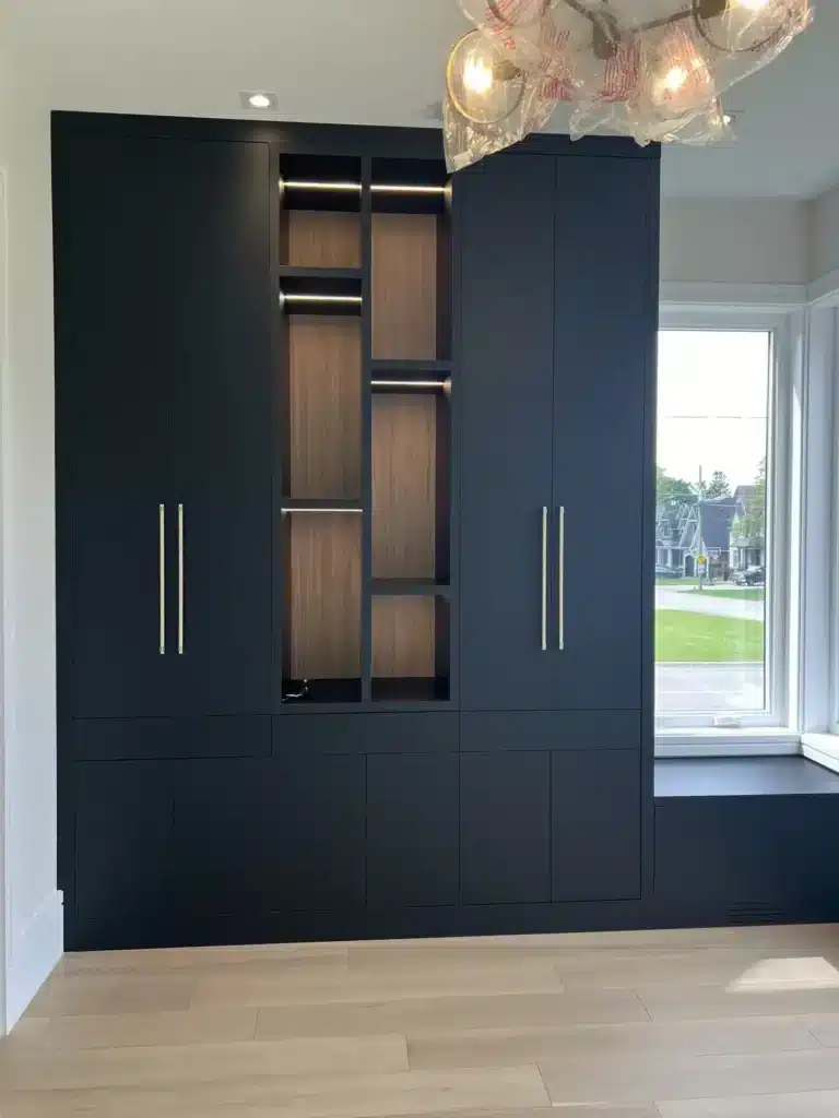 Custom kitchen design in an Ontario home: a navy built-in wall unit with brass pulls, a lit walnut display centre and a window seat.