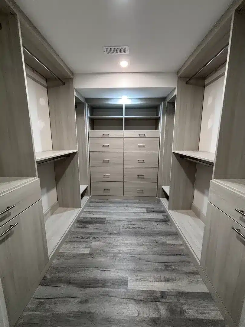 Basement walk-in closet in a greige woodgrain finish, double hanging on both sides and a ten-drawer bank at the end wall