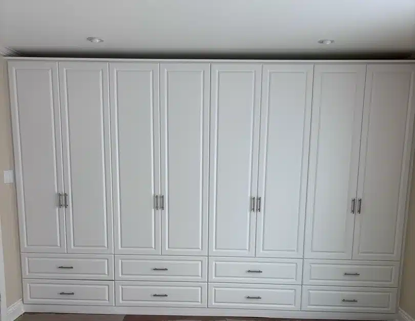 Cream wardrobe wall in Tiny Township with raised-panel doors, four double-door sections and two rows of drawers beneath