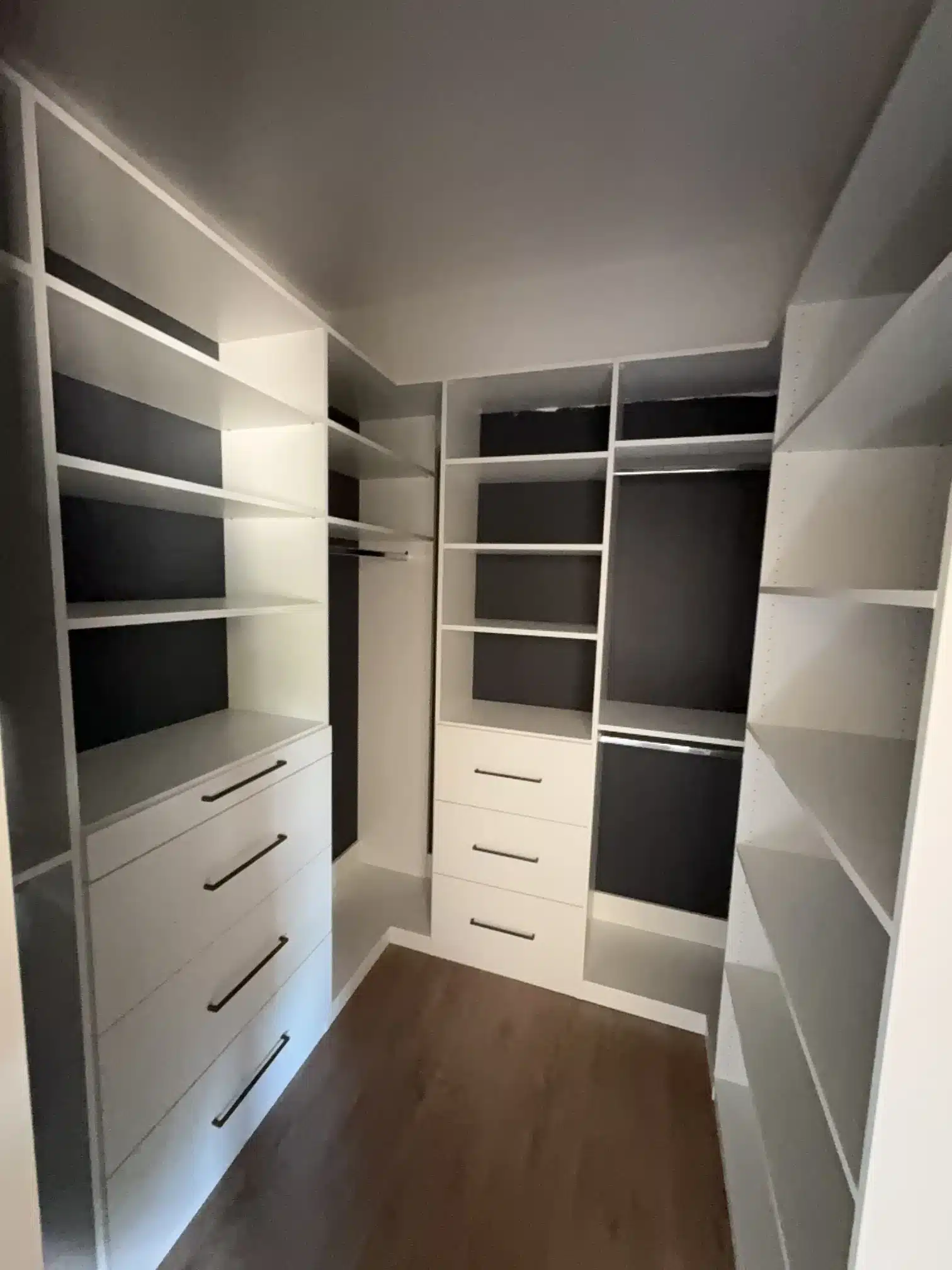 Four-walled white walk-in closet in Callander with shelving and hanging rods on every wall and two drawer banks