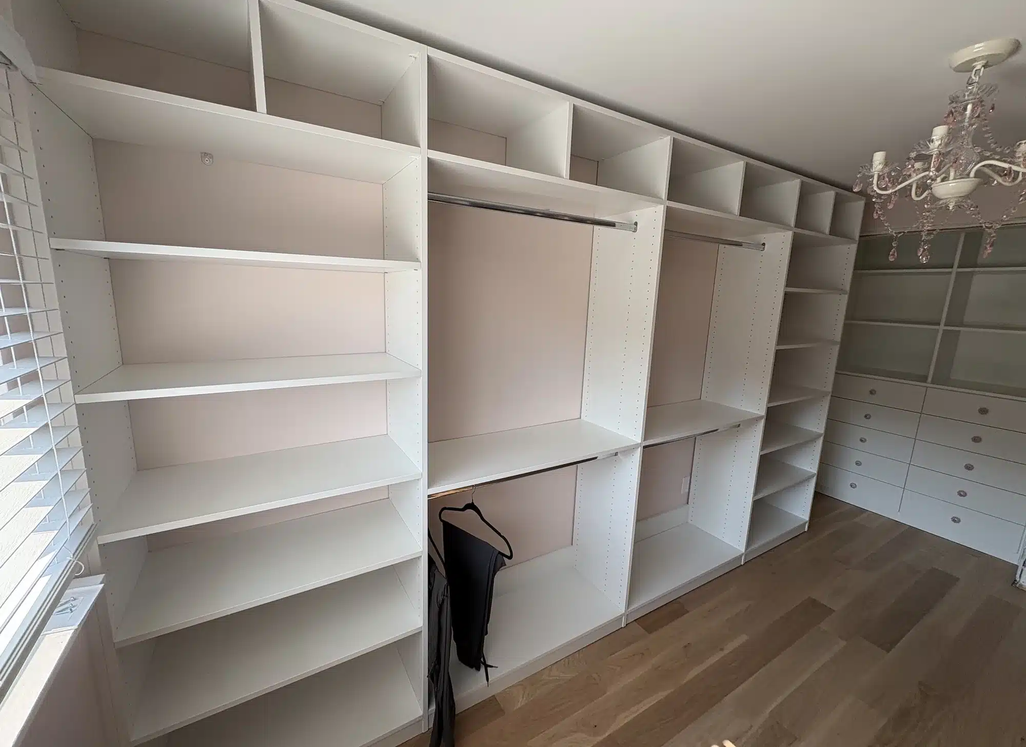 Full-room walk-in closet in Whitby with a wall of white shelving, double hanging rods and a chandelier