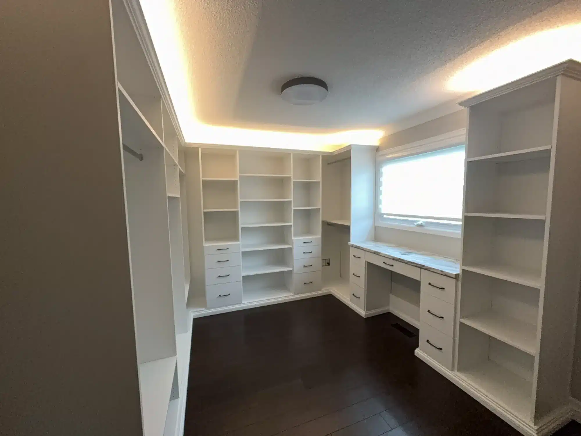Walk-in closet with cove lighting, a make-up vanity with a marble top, and shelving and hanging on three walls