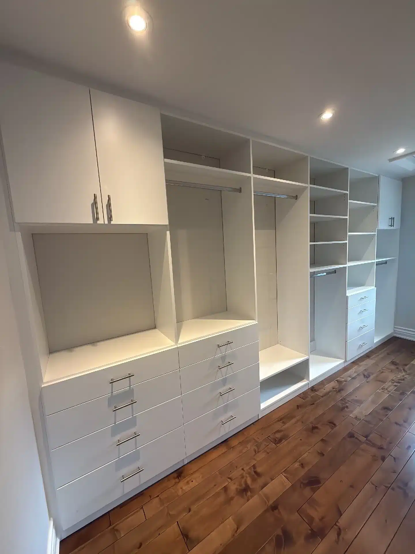 Full-wall white closet in Bolton with upper cabinets, two drawer banks, hanging sections and shelving under pot lights