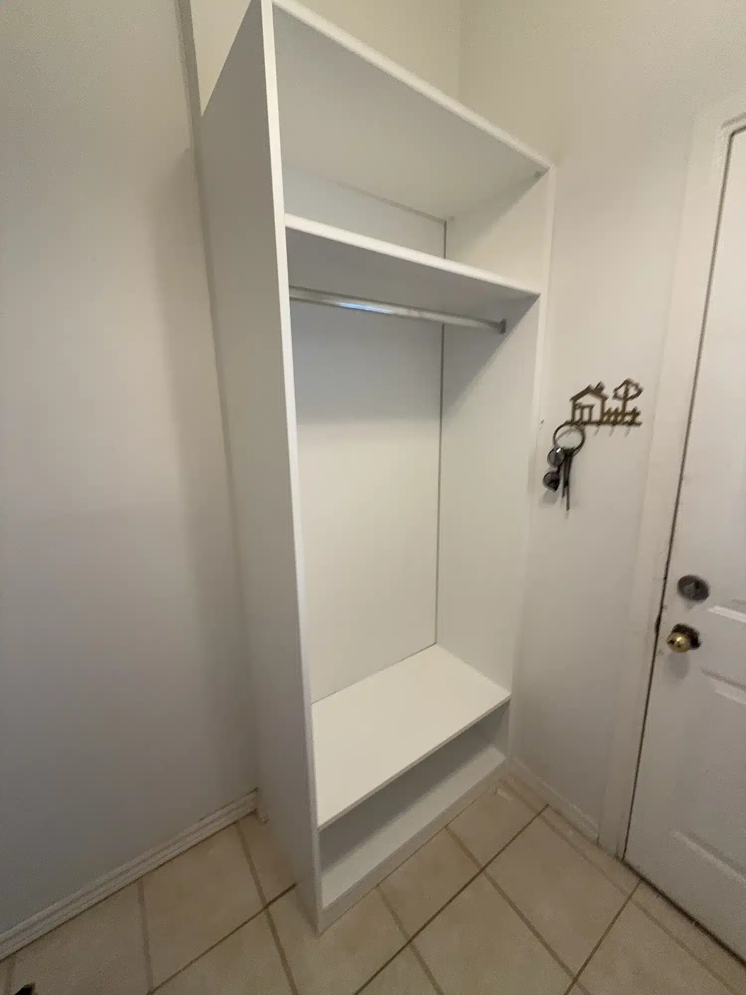 Open white coat tower beside a side door in a Toronto front hall, with a hanging rod, a top shelf and a low bench shelf for boots