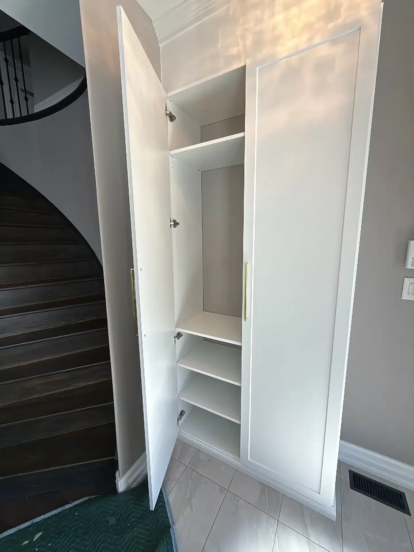 Tall white shaker-door cabinet built beside a curved staircase in a Toronto front hall, one door open to adjustable shelves